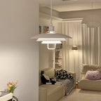 Lit from within, a white Clérachic pendant hangs in a corner above a sofa with patterned cushions and floor-length curtains.