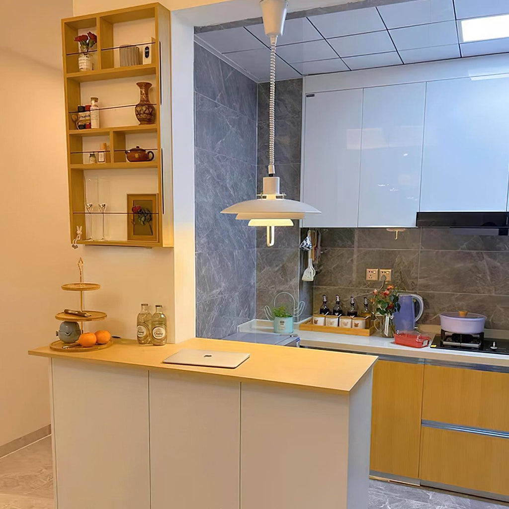 A white Clérachic pendant hangs above a kitchen counter with yellow wood cabinets and a shelf of ceramics behind.