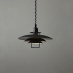Black Clérachic pendant against a mid-grey backdrop, with a white inner edge on each shade and a metal handle below.