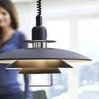 Close-up of the black Clérachic pendant's tiers and chrome-finish collar, with a blurred person and a bright window behind.