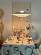 Over a dining table laid with candles and a floral cloth, a white Clérachic pendant gives a soft, warm light.
