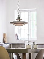 A black Clérachic pendant hangs in a bright kitchen, above a concrete-look table with glasses and two olive chairs.