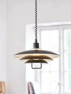 The black outer shade and lit white interior of this Clérachic pendant, seen near a tall paned window.