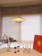 Candlelight and a red print sit below a warm-glowing Clérachic pendant, hung in front of white roller blinds.