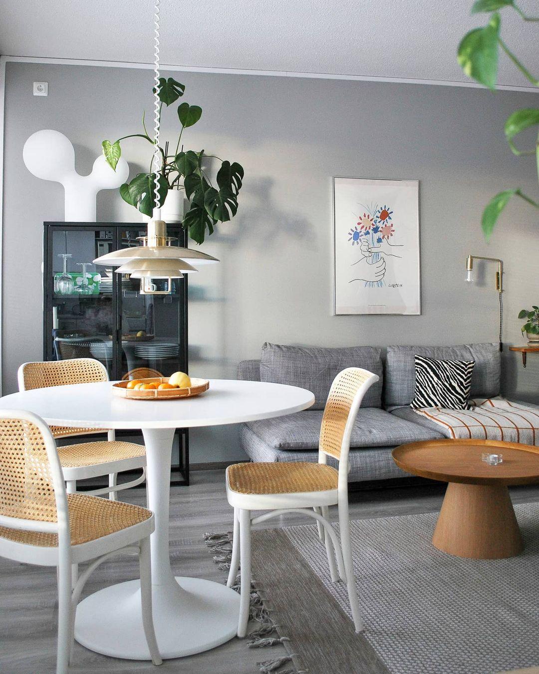 A small white Clérachic pendant hangs above a round white table with cane chairs, in a grey living room with plants.