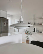 White Clérachic pendant in a bright kitchen with a steel fridge, hung low above a pale round table.