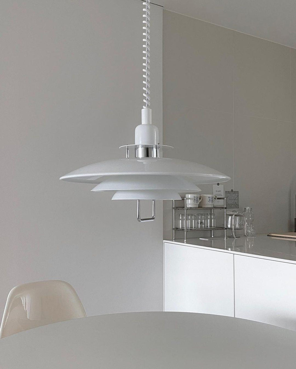 A white Clérachic pendant with a chrome-finish collar hangs over a kitchen counter, near a cream moulded chair.