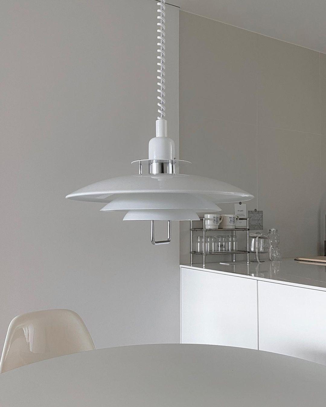 A white Clérachic pendant with a chrome-finish collar hangs over a kitchen counter, near a cream moulded chair.