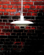 Against a dark red brick wall, a white Clérachic pendant stands out, its coiled cable dropping from above.