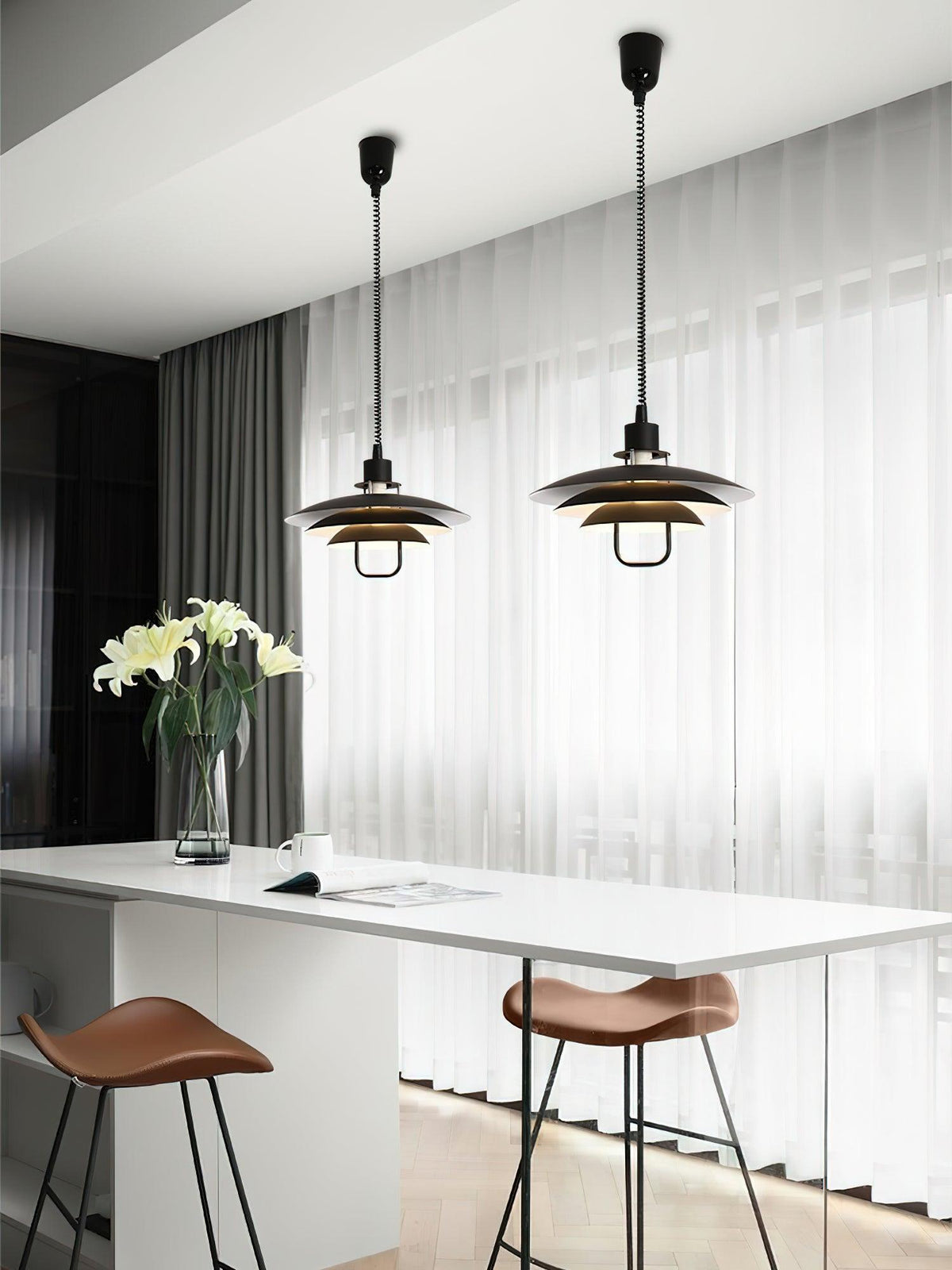 Two black Clérachic pendants with warm metallic inner shades hang over a white kitchen island with leather stools.