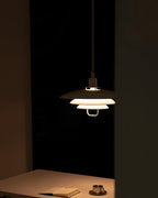 In a dark room, a Clérachic pendant lights a table with a notebook and a cup, its tiers glowing amber.