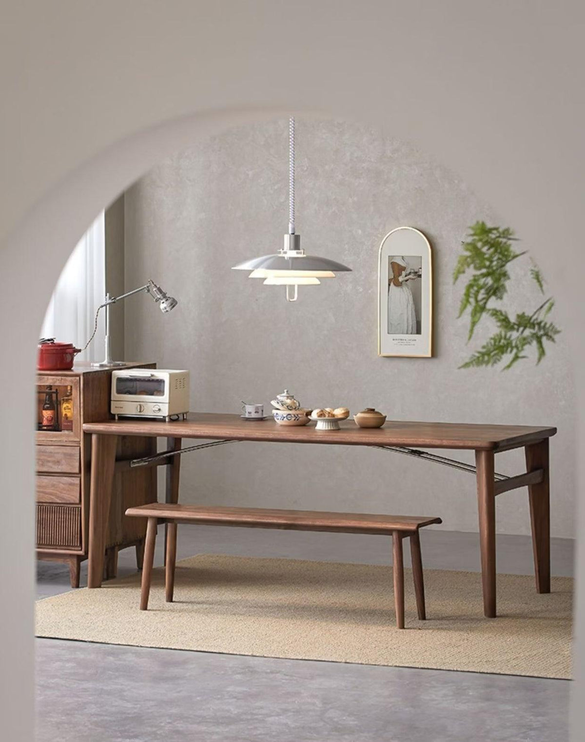 A small silver-grey Clérachic pendant hangs in an arched doorway, above a long walnut table with a bench.