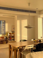 Late sun slants across a room where a Clérachic pendant hangs above a wooden table and a shelf of books.