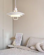A white Clérachic pendant hangs beside a bed with striped bedding, a framed line drawing on the side table.
