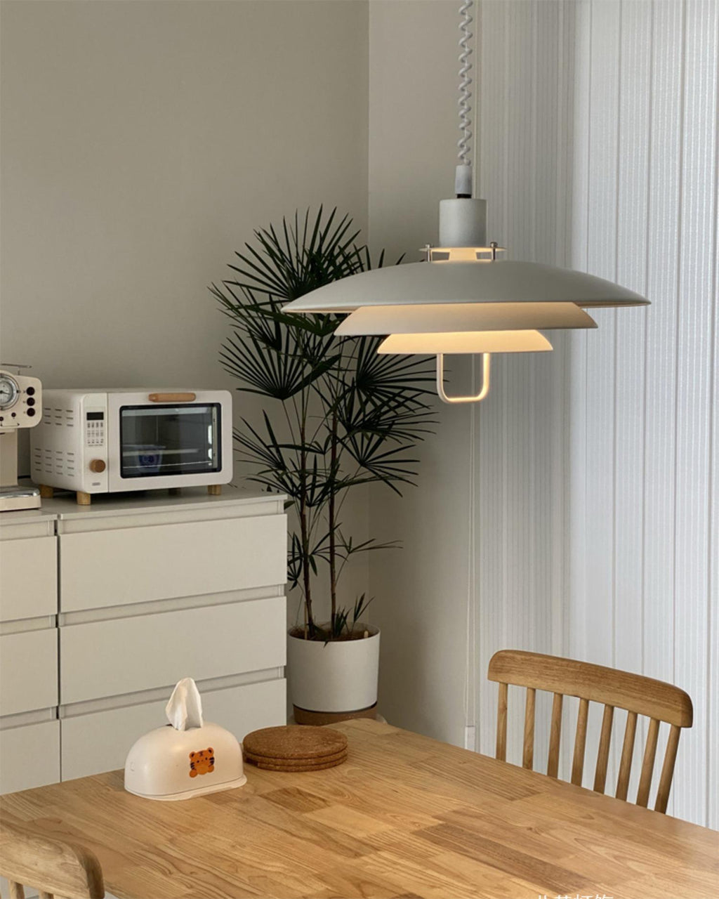 White Clérachic pendant seen from below its widest shade, above a pine table with a chest of drawers and a palm.