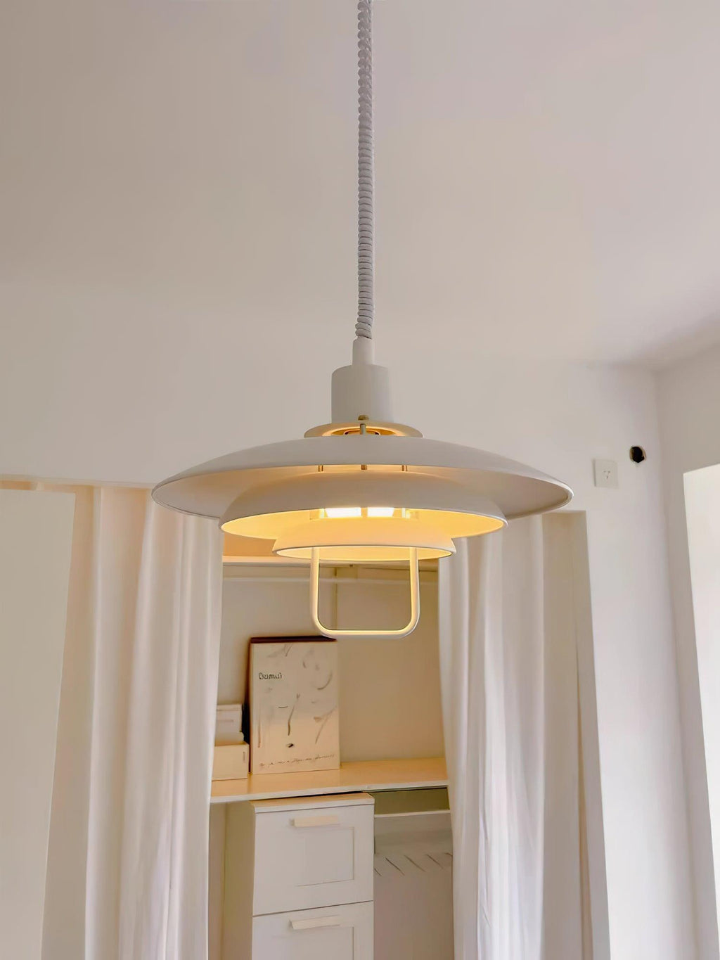 Hung between cream curtains, this white Clérachic pendant glows with a warm brass-toned inner edge.