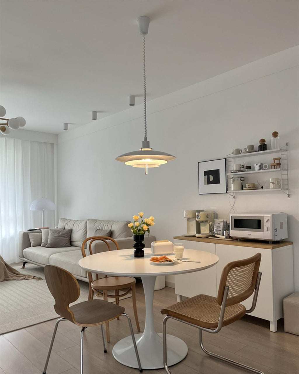 A white Clérachic pendant hangs in the centre of a compact living and dining space with a tulip-style table.