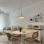 A wider shot of a living room where a white Clérachic pendant hangs over a round table with yellow flowers.