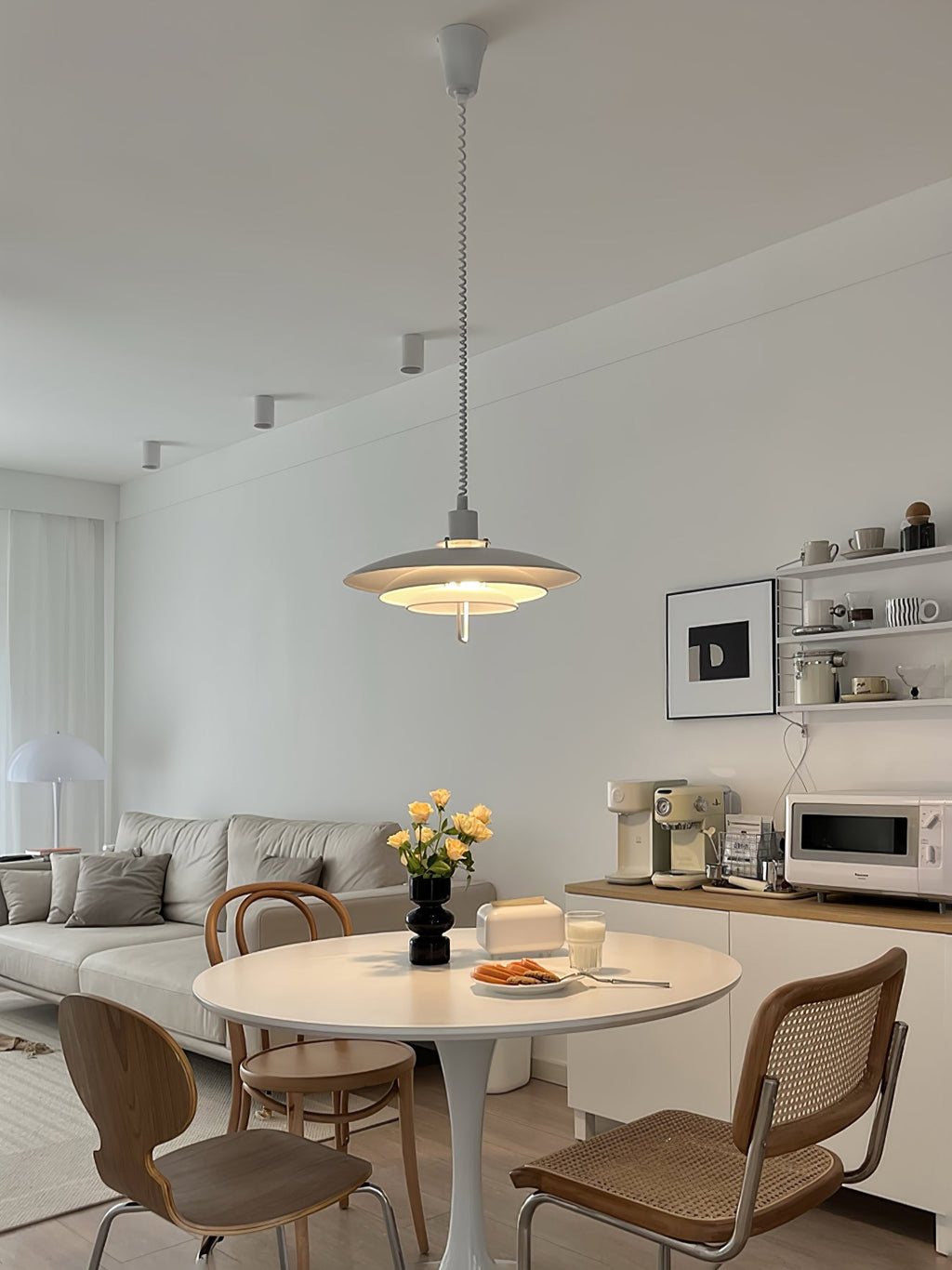 Seen from across the room, a Clérachic pendant hangs over a round table with cane chairs and open shelves.