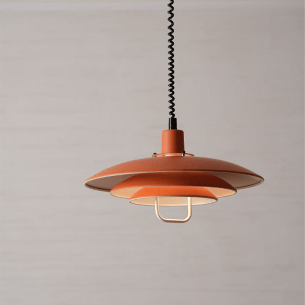 The orange tiers of this Clérachic pendant, with a cream inner shade and a white handle, on a soft grey-beige backdrop.