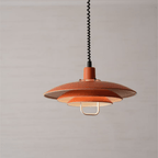 The orange tiers of this Clérachic pendant, with a cream inner shade and a white handle, on a soft grey-beige backdrop.