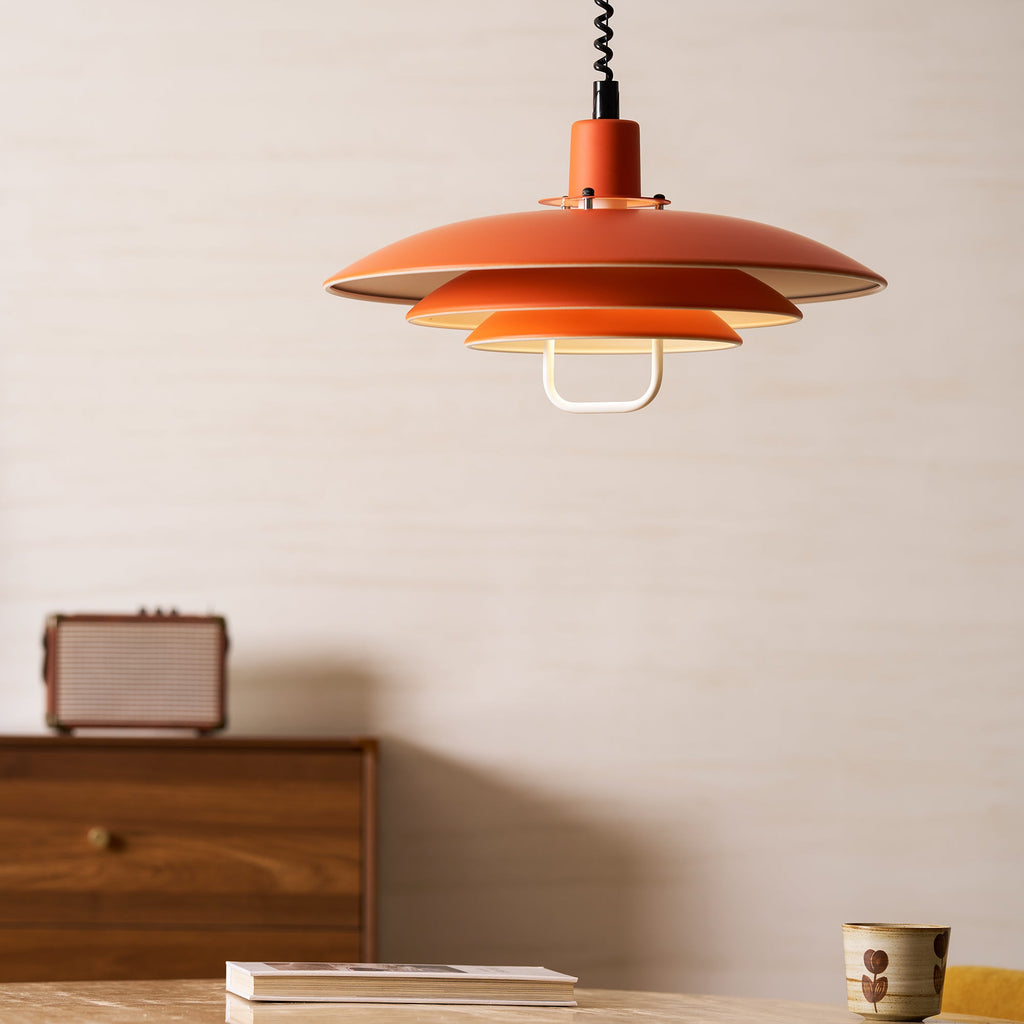This orange Clérachic pendant hangs level with a wood cabinet and a patterned cup on the table below.