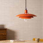 A smaller view of the orange Clérachic pendant, hung low beside a walnut cabinet and a book on the table.