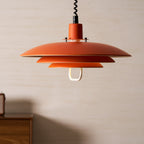 A wide orange Clérachic pendant hangs in front of a pale wall, with the black cable running up out of frame.