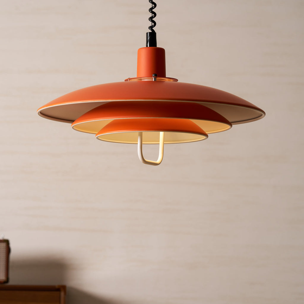 Orange Clérachic pendant seen from just below, its cream inner surfaces glowing against a pale wall.