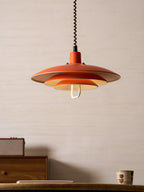 A neat orange Clérachic pendant hangs above a walnut drawer unit and a ceramic cup, with a pale wall behind.