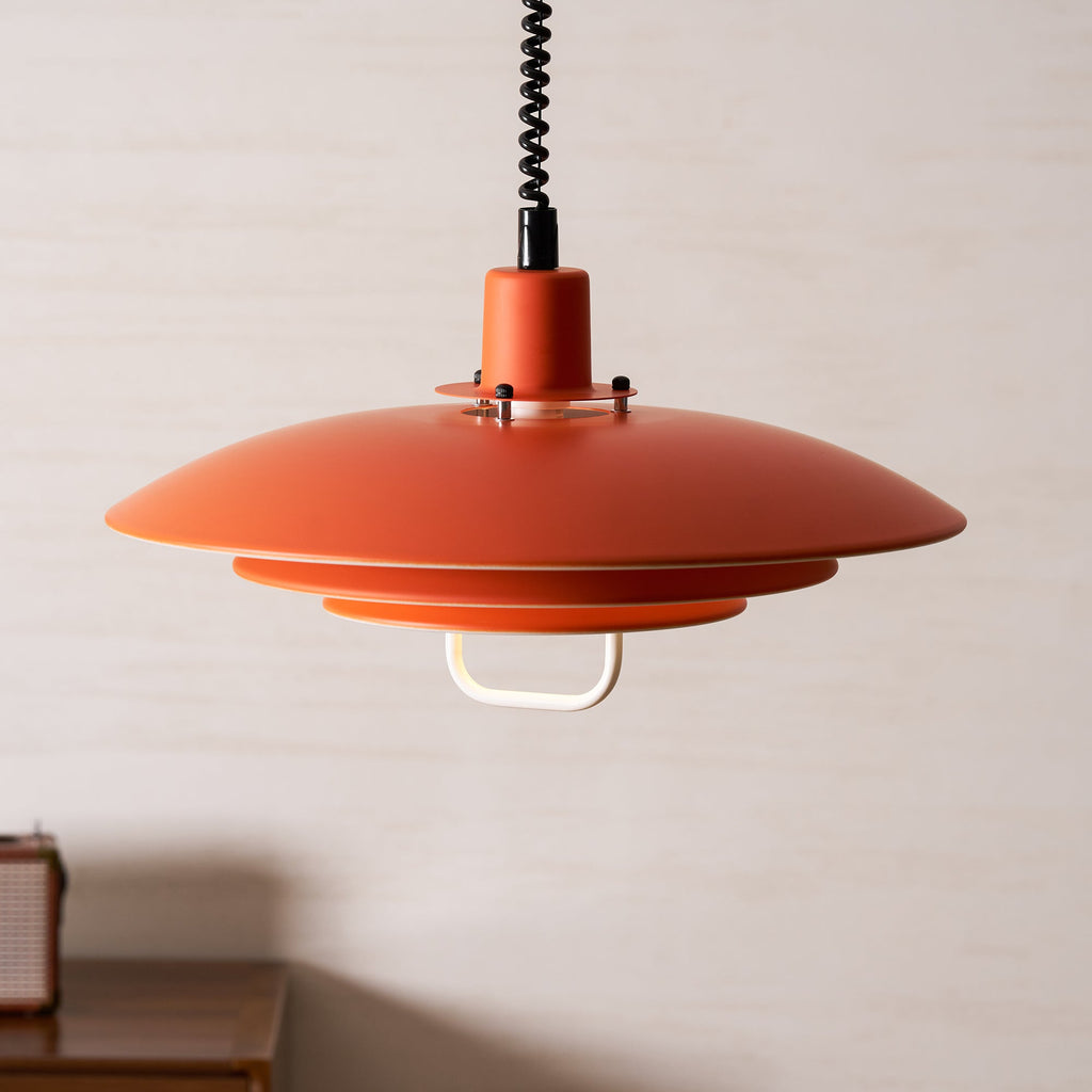 Looking up at the wide orange top shade of this Clérachic pendant, with the white handle below the lowest tier.