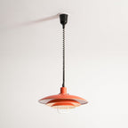 The same orange Clérachic pendant with its coiled cable shortened, from a black ceiling cup, lit inside.