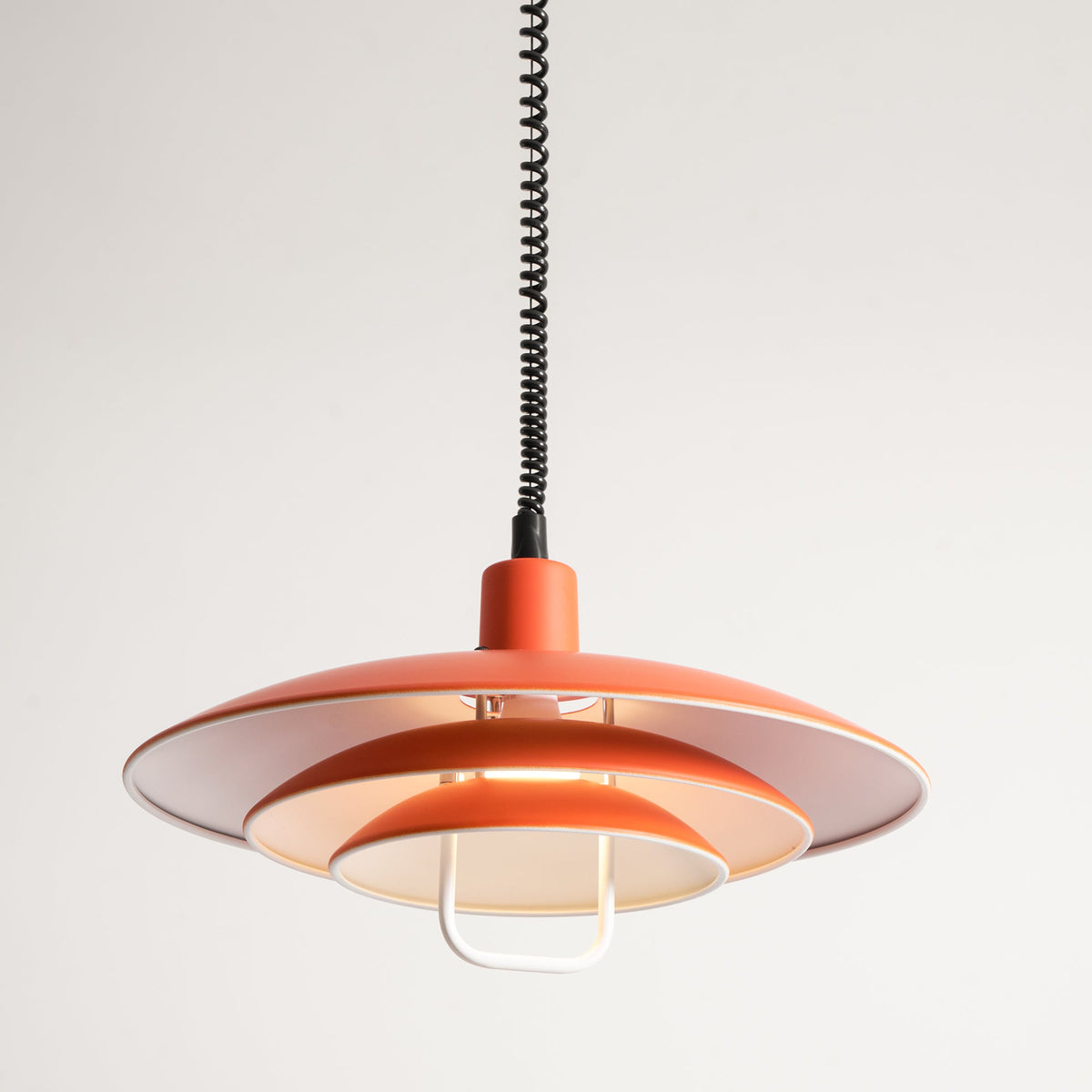 Close view of the orange Clérachic pendant's tiers from slightly below, with a cream interior and a white handle.