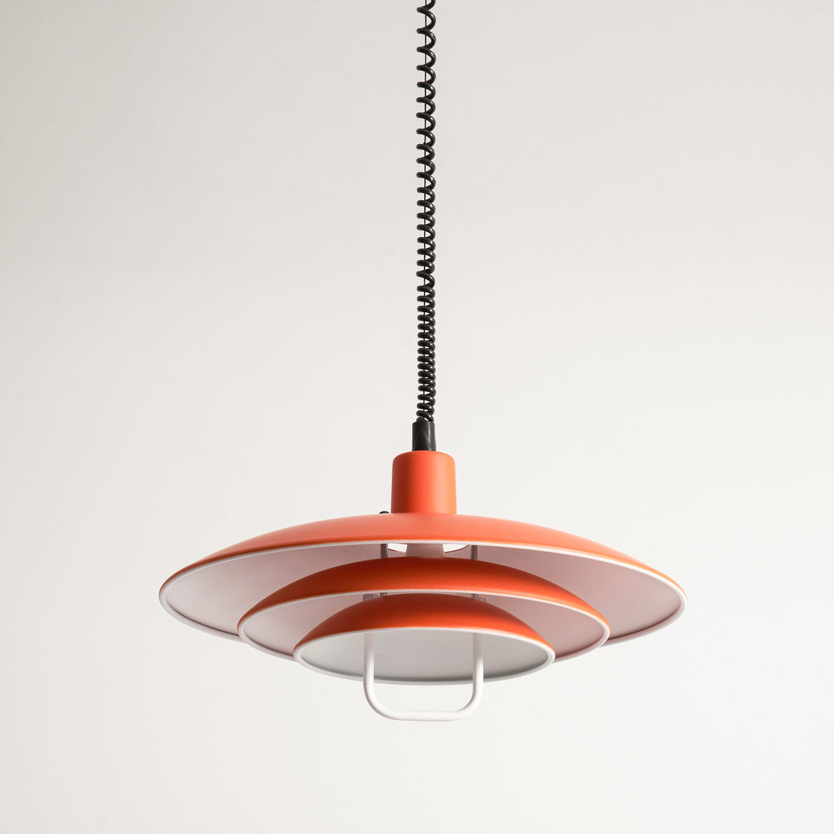 Orange Clérachic pendant from just below, showing the white inside of its broad top shade and the loop handle.