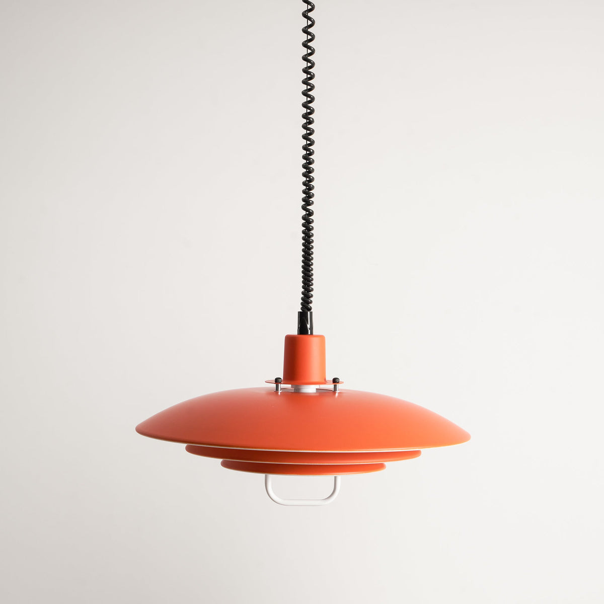 An orange Clérachic pendant on a pale backdrop, with a black coiled cable and a white loop handle below.