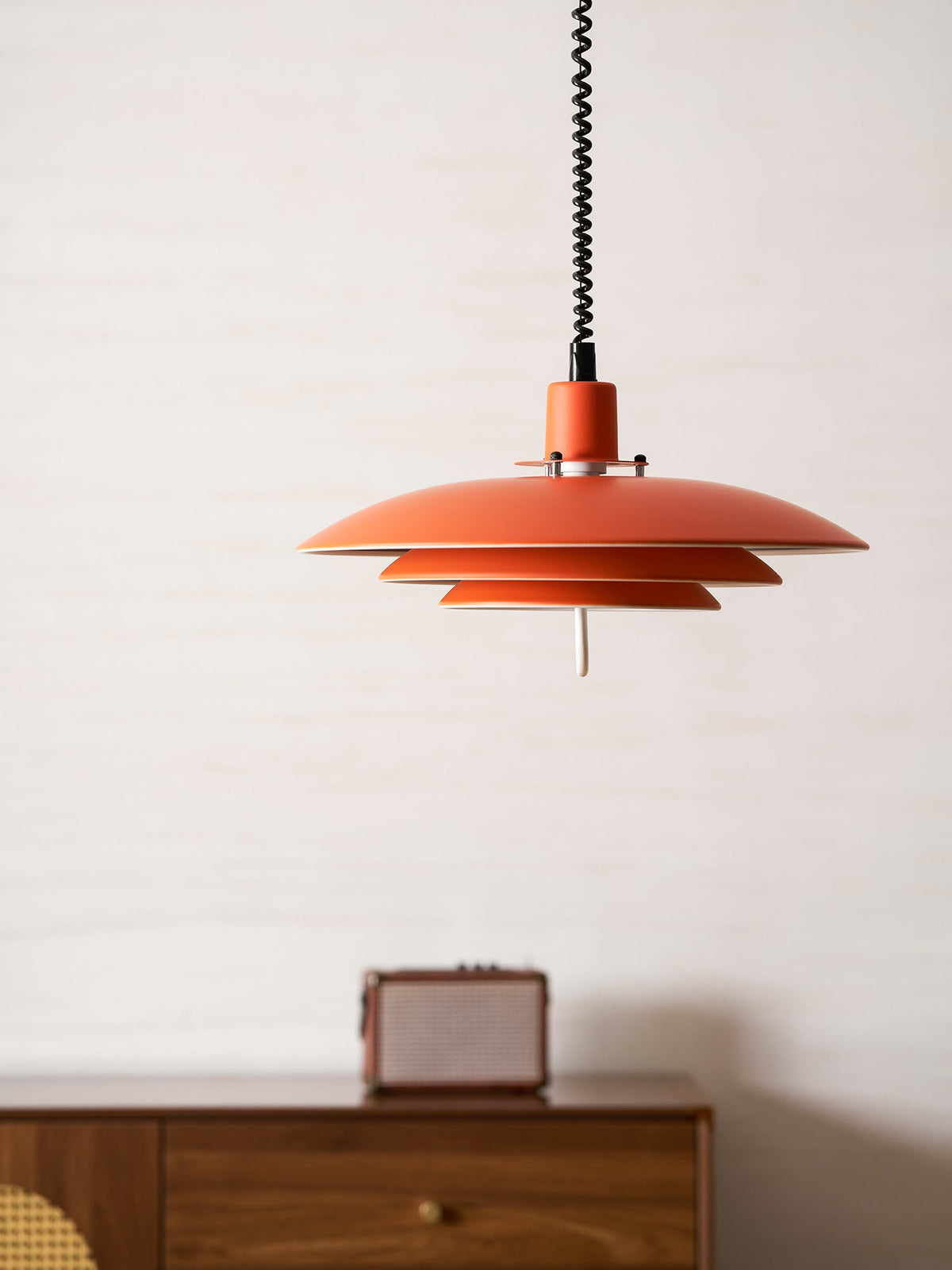 Orange Clérachic pendant seen from below, above a walnut sideboard with a small speaker.