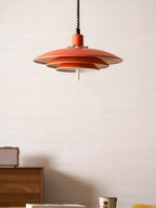 Orange Clérachic pendant with a cream inner edge, hung over a walnut cabinet with a cup and a book at the table.