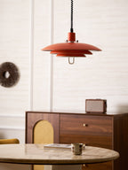 Orange Clérachic pendant seen from further back, with a round stone table, a rattan-fronted sideboard and a woven wall piece.