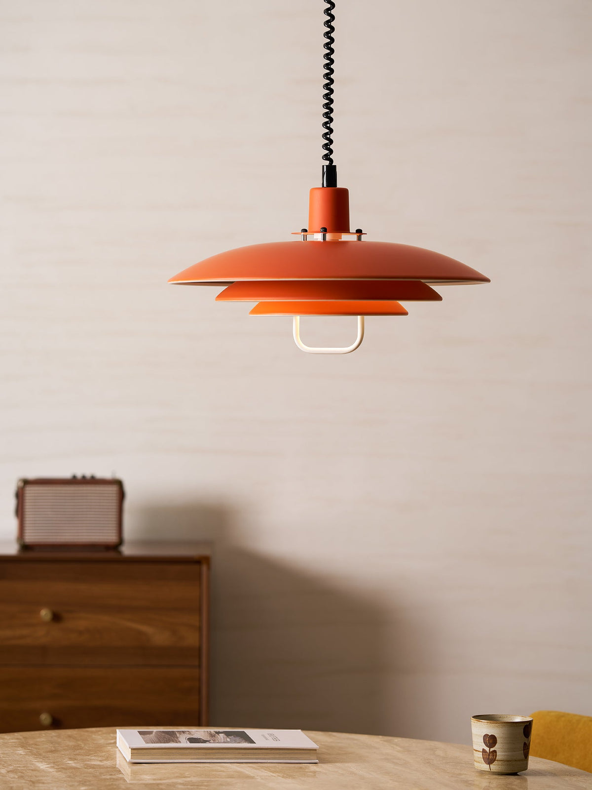 This orange Clérachic pendant sits above a walnut cabinet and a table with an open book and a small cup.