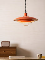 Lit from within, an orange Clérachic pendant glows warm in front of a pale wall and a walnut cabinet.