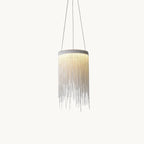 Lit Clérachic pendant with a cylinder of fine silver chains hanging on three thin cords against a plain off-white backdrop.