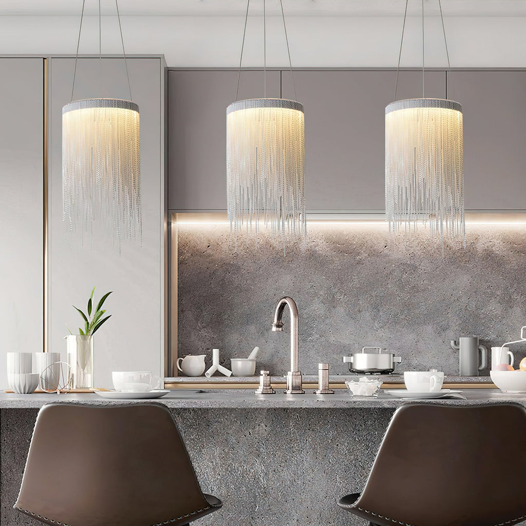 Three Clérachic chain-tassel pendants glow in a row above a grey kitchen island with brown bar stools.