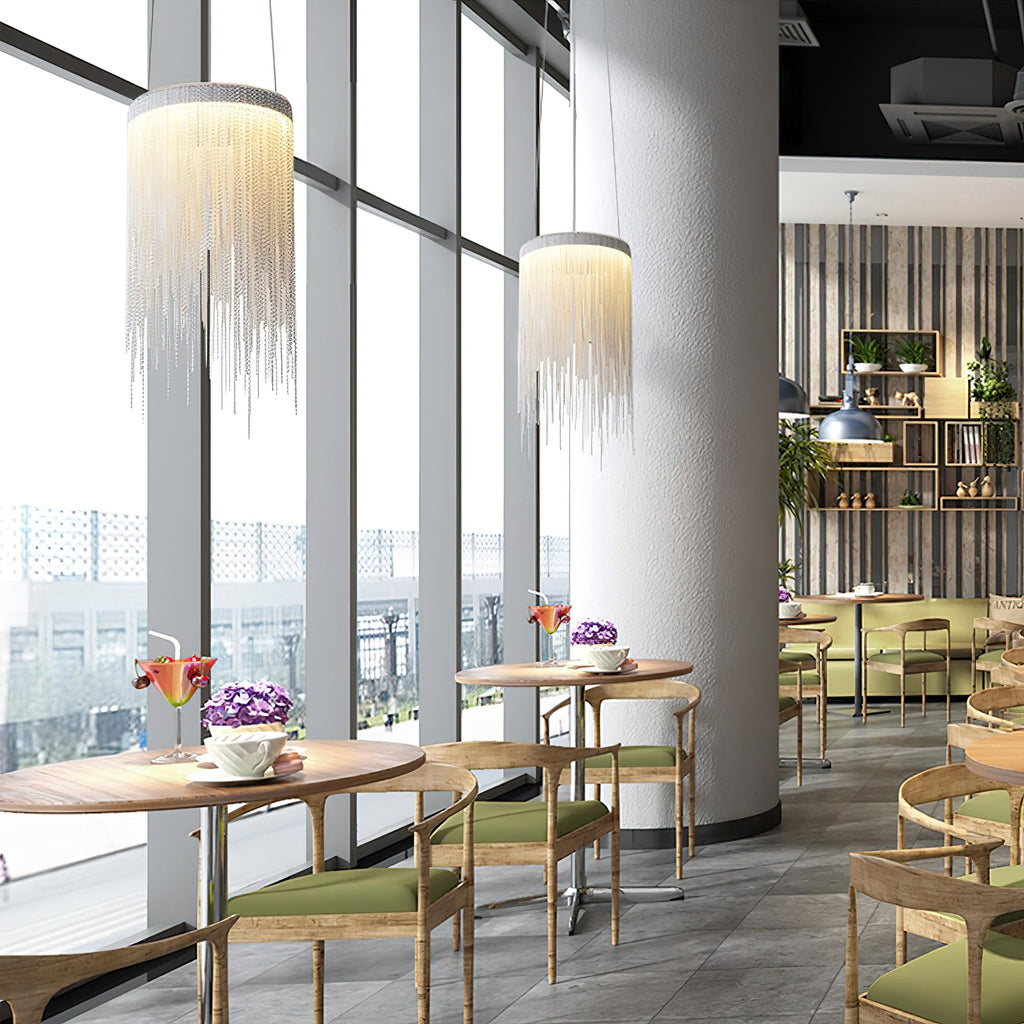 Two Clérachic silver chain pendants hang by floor-to-ceiling windows and a round column, with café tables and green chairs beyond.