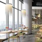 Two Clérachic silver chain pendants hang by floor-to-ceiling windows and a round column, with café tables and green chairs beyond.