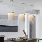 Three Clérachic pendants in a row above a dark dining table, each with a ring of warm light and chains falling below.