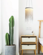 A single Clérachic chain pendant hangs beside a tall potted cactus and a pair of wooden drawers in a white room.