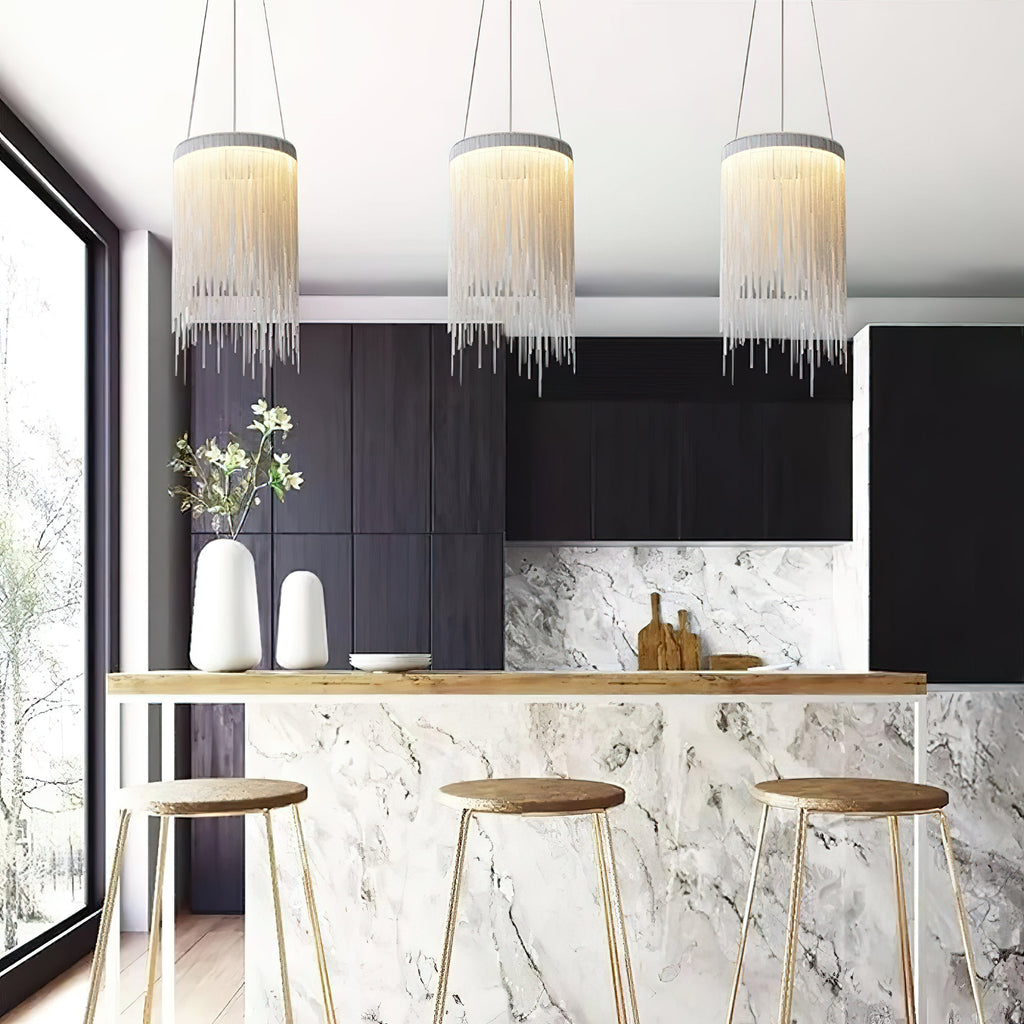 Three Clérachic chain pendants hang above a marble-fronted breakfast bar with wooden stools and a dark cabinet wall.