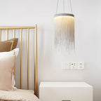 Clérachic chain-tassel pendant beside a brass-framed bed with blush cushions and a white bedside unit.