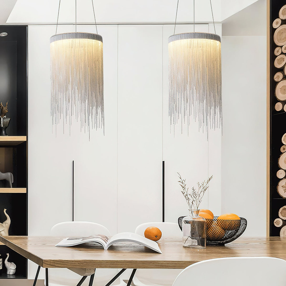 Two Clérachic chain pendants in a dining room with a wooden table, an open book, a wire fruit bowl and white cabinets.