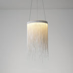 Clérachic silver chain pendant lit against a soft grey wall, its light ring glowing above the hanging strands.